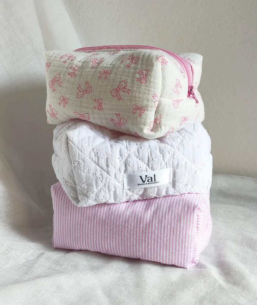 Selezione estiva 2025. Beauty case handmade con tessuti fantasia rosa e pizzo sangallo, e gioielli in acciaio inossidabile con ciondoli che richiamano l'estate Italiana.