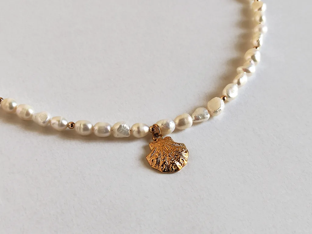 Collana di perle con ciondolo marino. Particolare della collana con ciondolo centrale, a forma di conchiglia dorata.